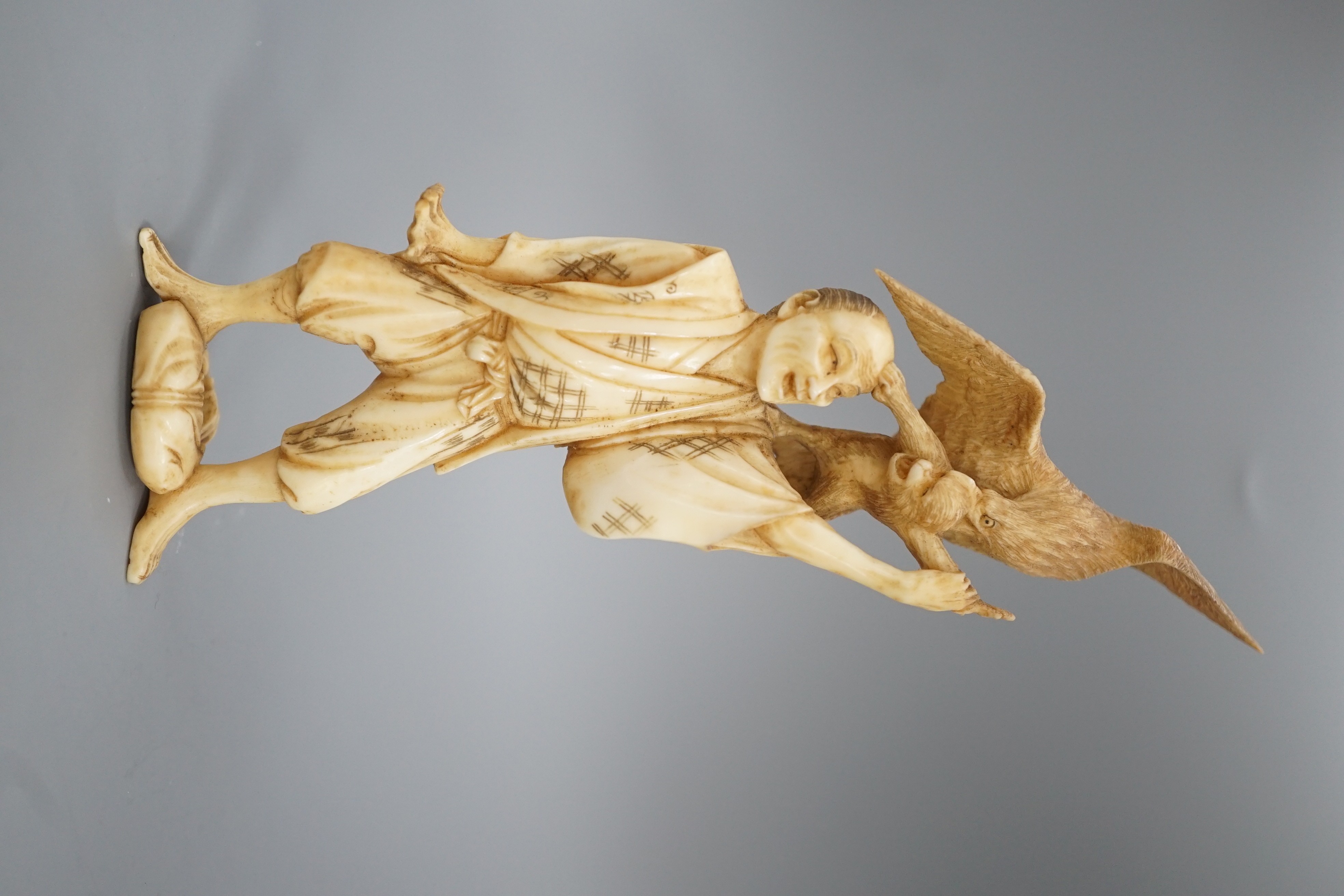 A Japanese ivory okimono of a man holding a monkey which is being attacked by an eagle, early 20th century 15.5cm